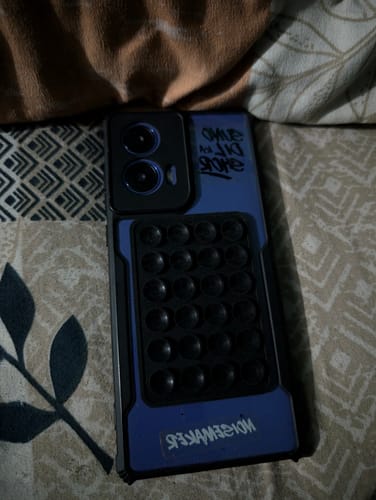 Customer's black StickyPod attached to the back of a blue smartphone case, resting on a patterned surface.