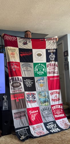 Customer holding up their large, multi-colored Project Repat T-Shirt Quilt in a living room.