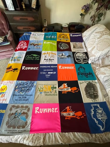 Customer's colorful Project Repat T-Shirt Quilt made from running race shirts, spread out on a bed.