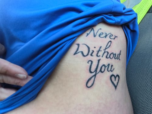 Customer lifts their blue shirt to show a new tattoo on their side, with calm skin after using the numbing cream.