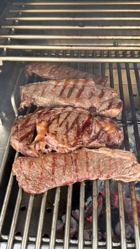 Cliente asando varios steaks de Diezmillo jugosos sobre una parrilla caliente.