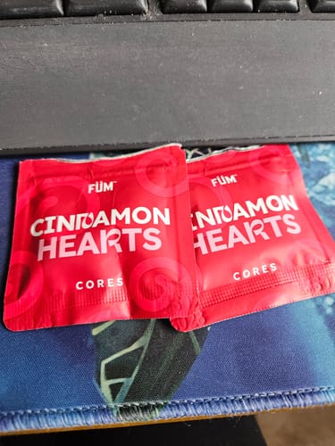 Customer's two red foil packets of Cinnamon Hearts Cores sitting on a desk mousepad.