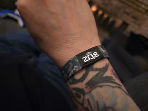 Customer's tattooed wrist wearing the camo-pattern Iron Sharpens Iron Bible Verse Bracelet.