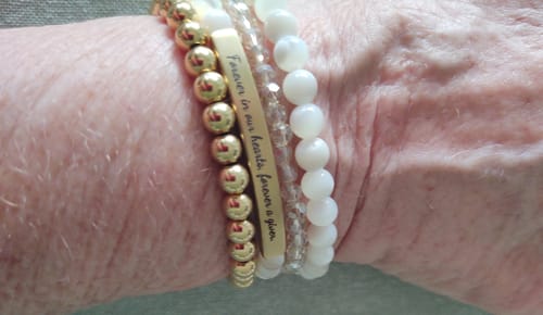 Close-up of a customer's wrist wearing the stacked Mother Of Pearl Custom Bracelet with an engraved gold bar.