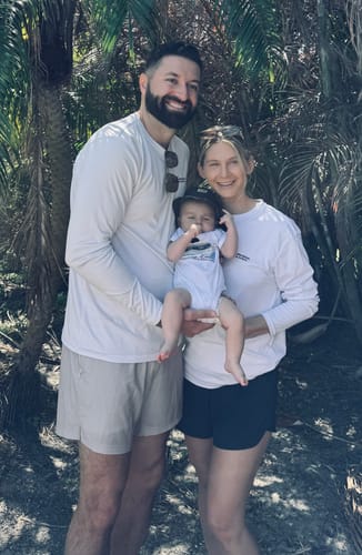 Reviewer and another person holding a baby wearing the white custom cotton onesie outdoors.