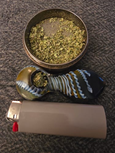 Customer's White Runtz ground in a grinder and packed into a colorful glass pipe with a lighter.