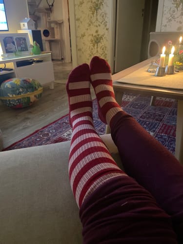 En kund kopplar av på en soffa med fötterna uppe, iklädd röd- och vitrandiga Diasocks stödstrumpor.