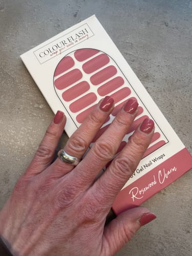 Kundin zeigt ihre fertige Maniküre mit glänzenden „Rosewood Charm“ UV-Gel-Nagelfolien über der Produktverpackung.