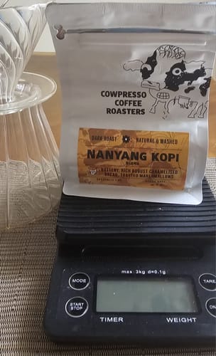 Customer's bag of Nanyang Kopi Roast on a black digital scale next to a pour-over brewer.