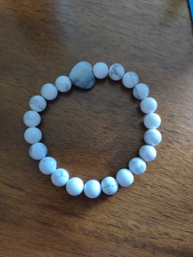 Reviewer's crystal bracelet with white marbled beads and a grey heart-shaped accent stone on a wooden surface.
