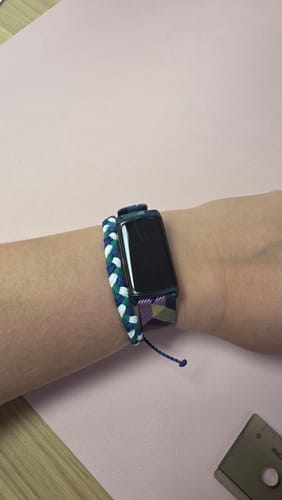 Customer wearing the woven DAVID Bracelet in blue, green, and white on a wrist next to a smartwatch.