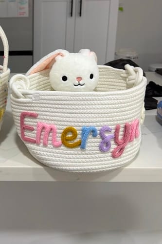 Reviewer's white personalized knitted basket with the name 'Emersyn' in multicolor yarn, holding a white stuffed bunny.