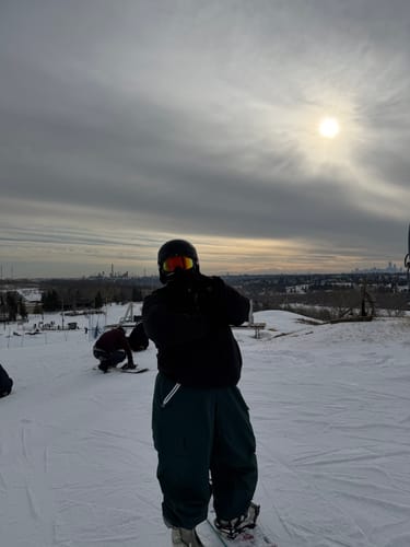 Reviewer on a snowboard wearing the dark green baggy snow pants on a snowy hill.
