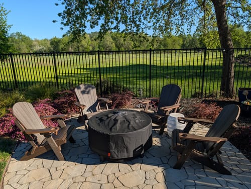 Customer's set of four woodgrain Adirondack chairs arranged around a fire pit on a sunny patio.