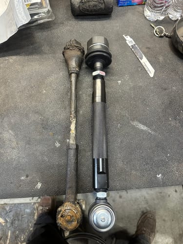Customer comparing a new Heavy Duty Tie Rod Kit to an old, rusty original part on a workbench.