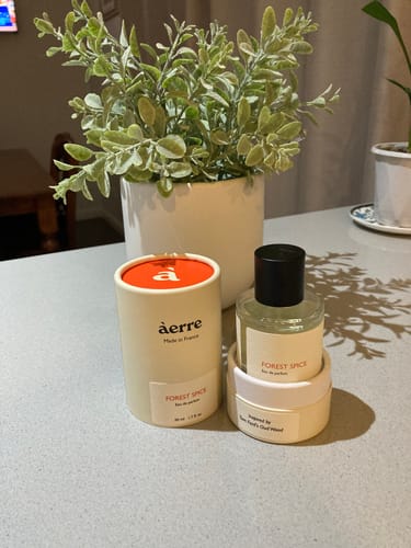 Customer's Forest Spice perfume bottle and packaging on a countertop next to a potted plant.