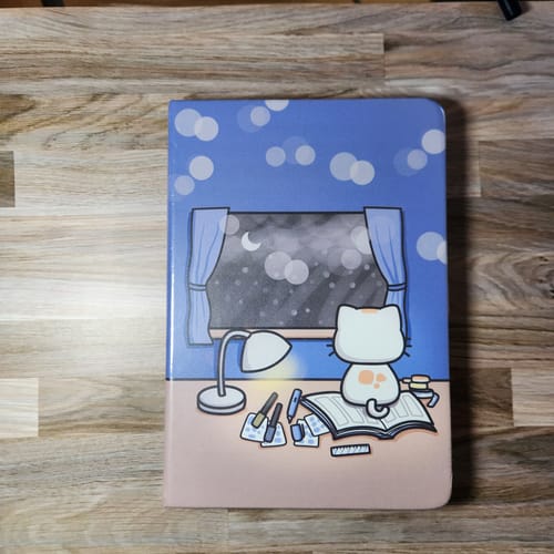 Customer's Cozy Cat Journal on a wooden surface, showing the illustrated cover of a cat studying at a desk at night.