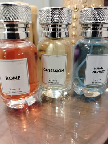 Customer's three Signature Perfumes bottles: Rome (orange), Obsession (yellow), and Nanga Parbat (blue) on a table.