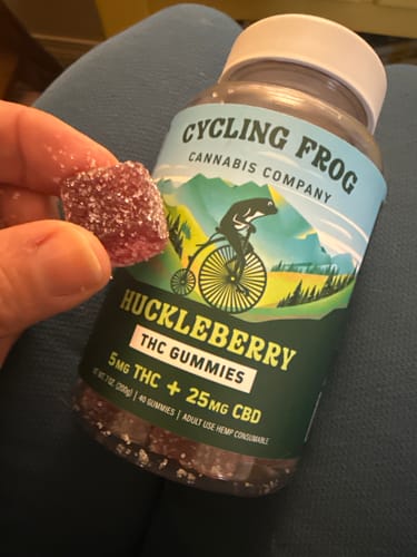 Reviewer holds a sugar-coated Huckleberry Gummy next to the bottle, showing the product label and other gummies inside.