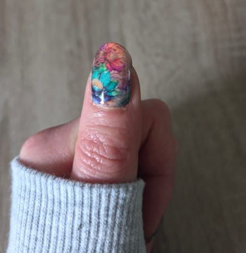 Nahaufnahme des Daumens einer Kundin mit der bunten Nagelfolie „Rainbow Forest“.