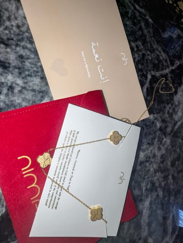 Reviewer's gold Sabr, Shukr, Tawakkul Necklace displayed with its red pouch and cards on a marbled surface.