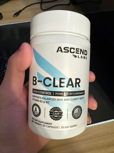 Customer holding a white bottle of B-CLEAR skin supplement in their hand.