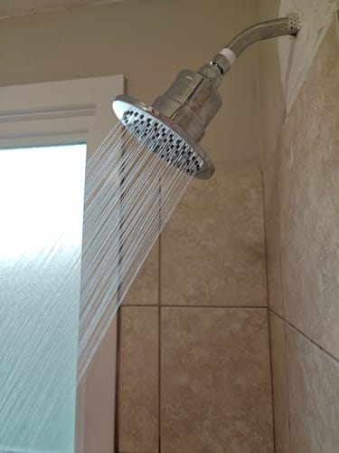 Customer's shower head with the inline filter installed, spraying water in a tiled shower.