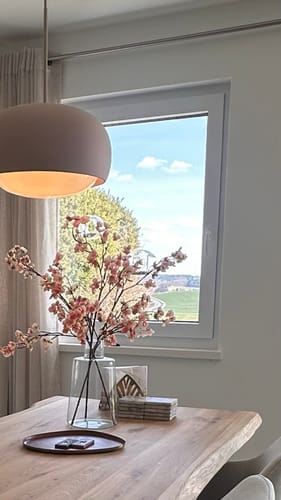 Recensent toont de oudroze Zijden Bloesem in een glazen vaas op een houten tafel.