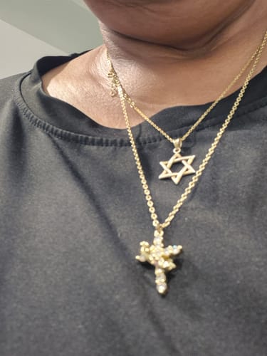 Close-up of a customer wearing the gold-colored Crowned in Faith Cross Necklace, layered with other necklaces.