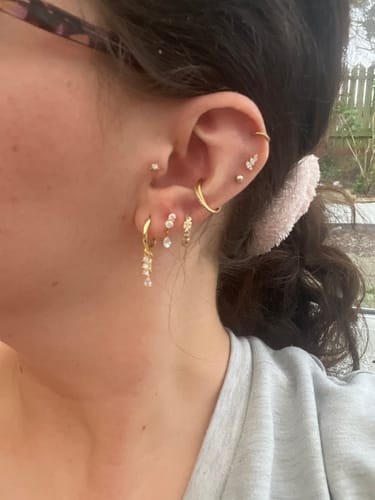 Customer's ear showing the Small Solitaire flatback Gold stud in their tragus piercing, styled with other gold earrings.
