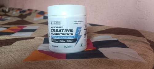 A customer's white tub of Wellcore Micronised Creatine Monohydrate placed on a patterned bedspread.