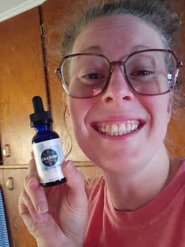 A smiling reviewer holds up the small, blue bottle of Meraki Blu Methylene Blue.