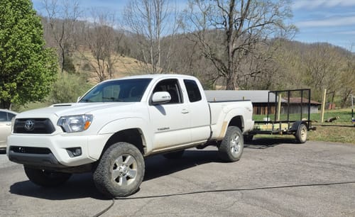 Reviewer's white Toyota Tacoma with the leveling lift kit installed, parked and hitched to a utility trailer.