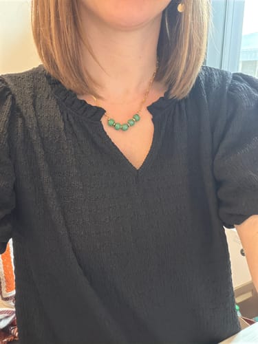 Reviewer wearing the Bel Koz Gold Single Strand Clay Necklace with green beads against a black blouse.