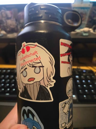 A customer holds up a black water bottle covered in several durable custom stickers.