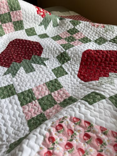 Customer's finished Strawberry Fields Quilt showing the patchwork strawberry design and detailed quilting stitches.