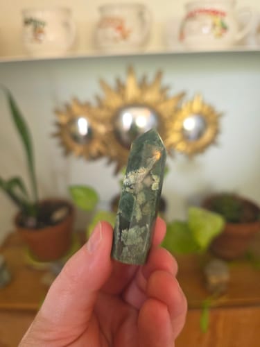 Customer's hand holding a green and white moss agate crystal tower.