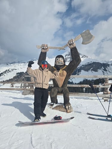 Reviewer posing on a snowboard in a light-colored snow jacket on a snowy mountain.