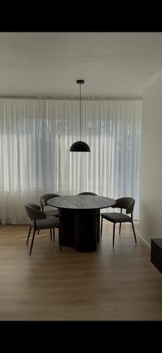 Recensent toont de zwarte Bloop hanglamp die boven een ronde, donkere eettafel hangt.