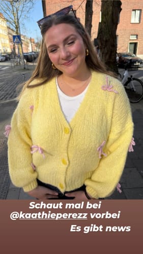 Kundin trägt den gelben Oversize Mini Schleifen Cardigan mit rosa Schleifen im Freien.
