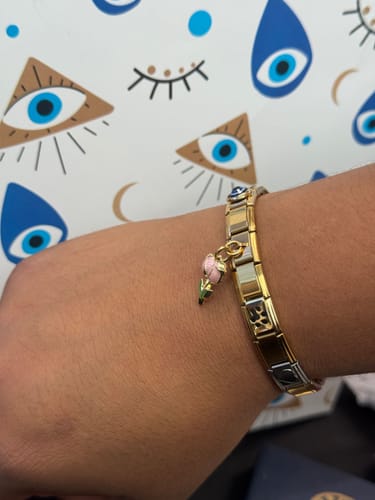 Cliente mostrando su pulsera italiana de dos tonos en la muñeca, con un charm colgante de flor.