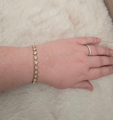 Eine Kundin zeigt das goldfarbene Drop Heart Armband, das sie am Handgelenk trägt.