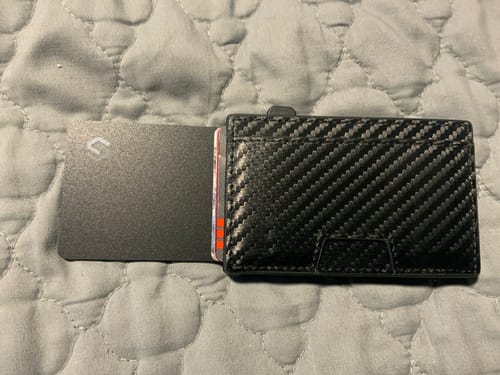 Customer's SPOTMINDERS Tracking Card PRO partially inserted into a black carbon fiber wallet, shown on a quilted surface.