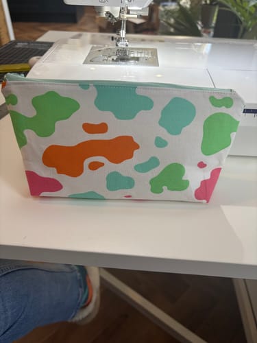 Customer's finished DIY bag, featuring a colorful cow print, sitting in front of a sewing machine.