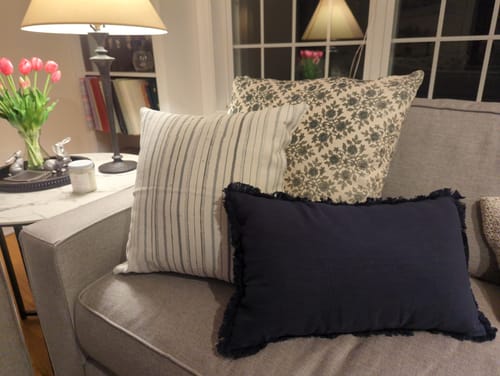 Customer's Mack in Linen pillow styled on a grey sofa with a dark blue and a floral pillow.