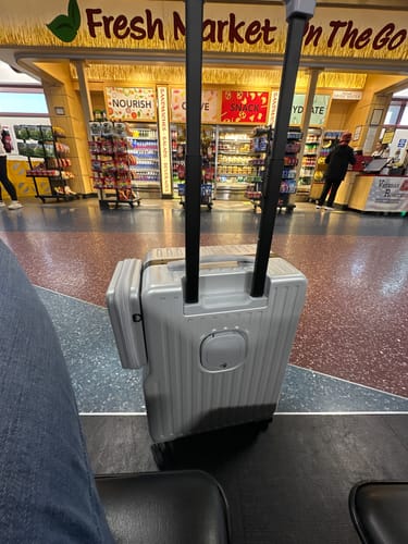 Customer's silver Duo-Carry luggage with its side bag attached, standing on the floor in an airport terminal.