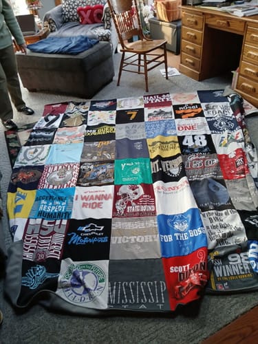 A customer's large Premium T-Shirt Quilt, made from many different t-shirts, spread out on a living room floor.