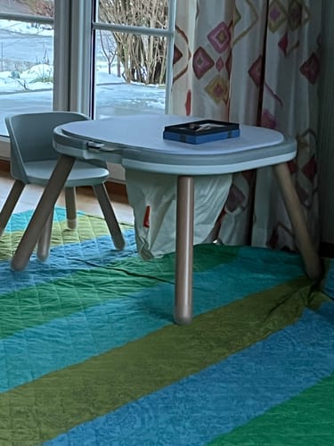 Ein Kunde zeigt das aufgebaute Funzy Spieltisch Set mit Stuhl in einem Zimmer auf einem bunten Teppich.