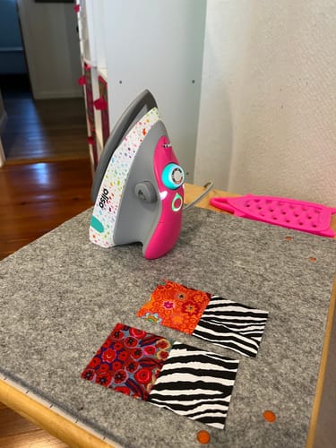 Customer's pink Oliso Mini M3Pro Project Iron on a wool mat with two small quilt blocks.