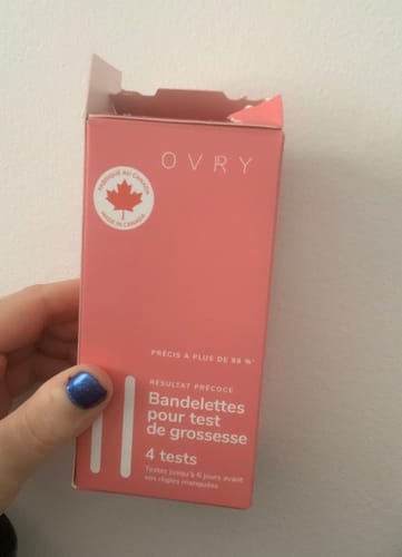 Customer holding the pink, French-language box of Ovry Pregnancy Test Strips.